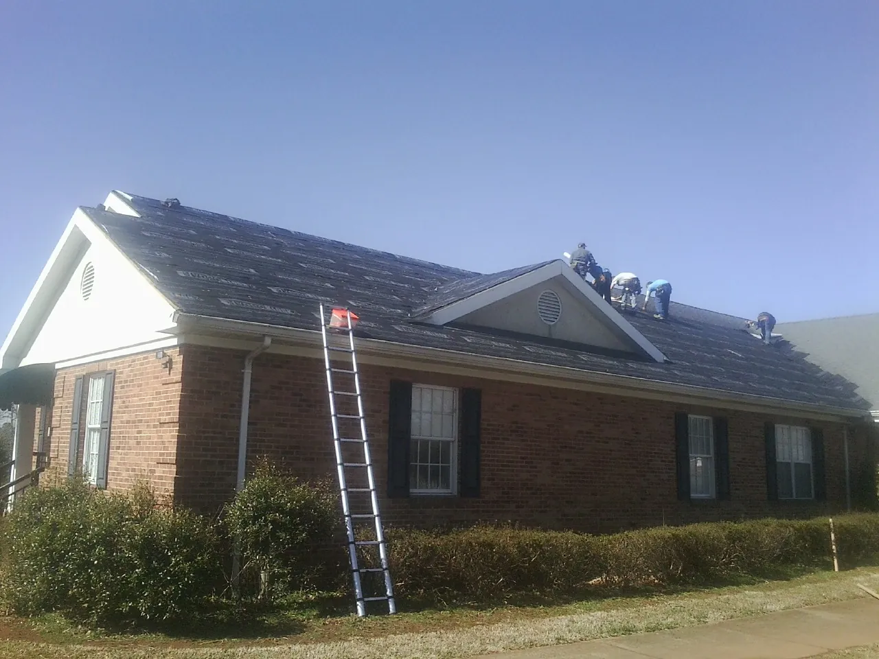 Crew tearing shingles off a brick ranch roof with a ladder set — Metal Roof Repair work by our crew in Newtown