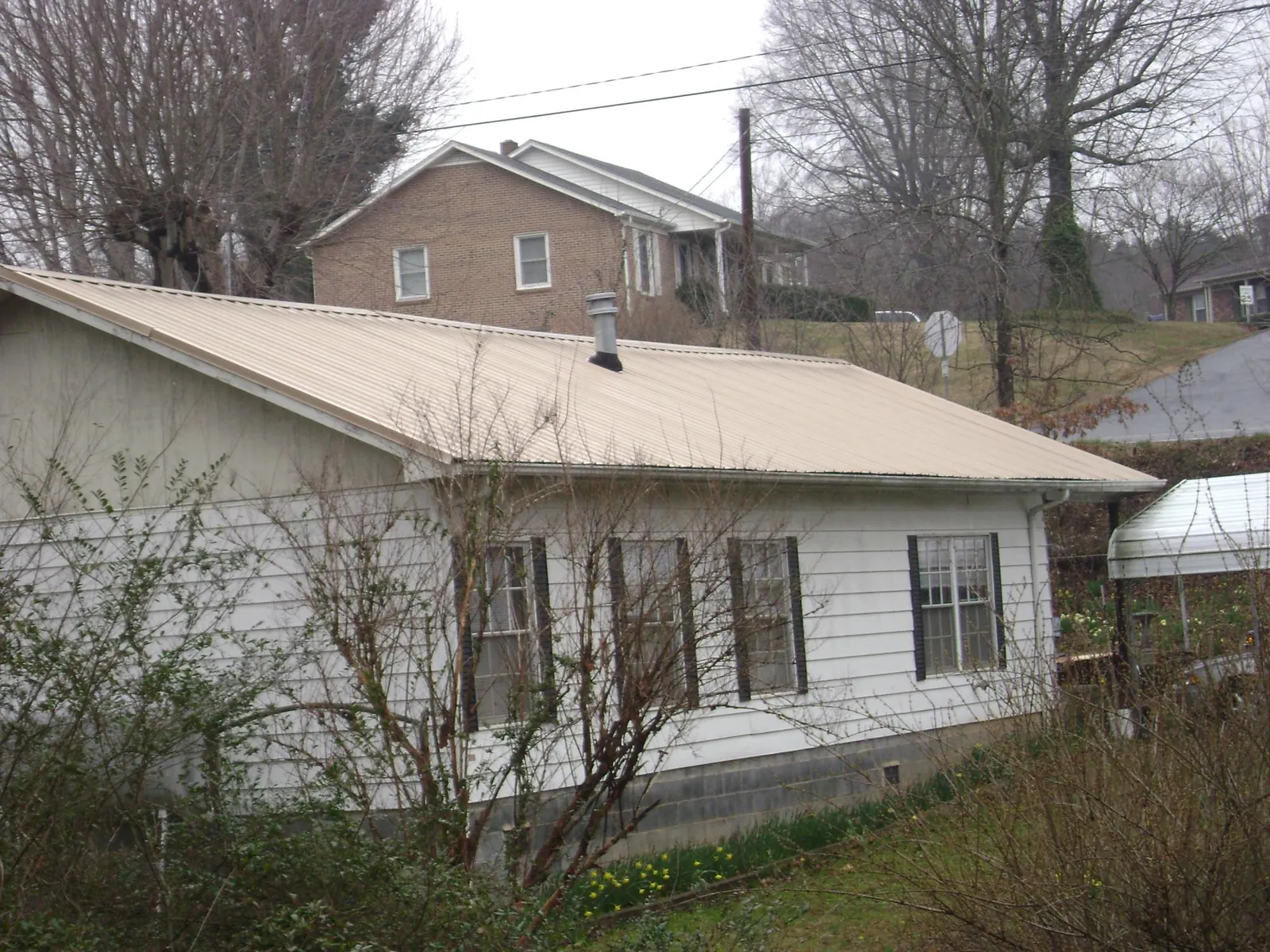 Tan metal roof on a white sided house set into a hillside — Commercial Roofing by Roofing Brothers in Newtown